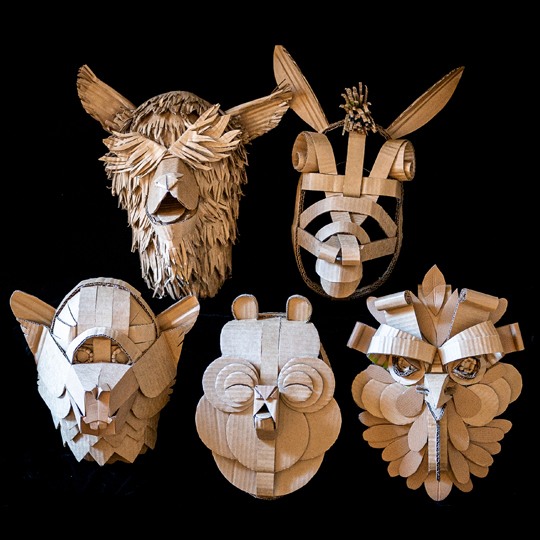 Photo of a set of five cardboard animal masks on a black background, the first looks like a sheep, second a donkey, third a rat like creature, fourth a bird like animal nd fifth an owl